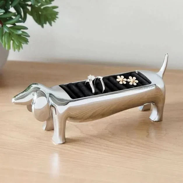 Dog-shaped ring holder with rings on a wooden surface next to a plant